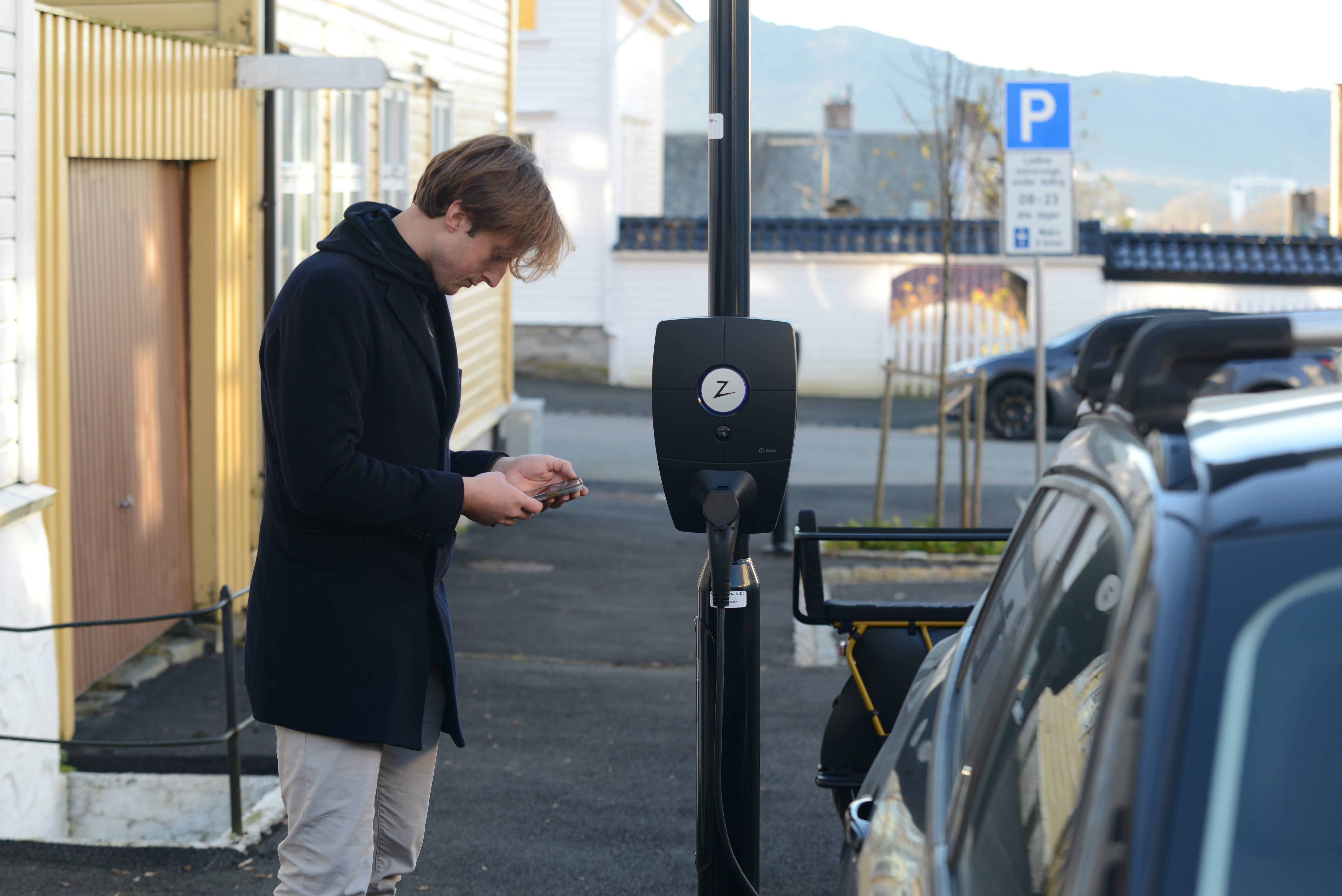 Mann som laaser opp elbillader med mobilen sin